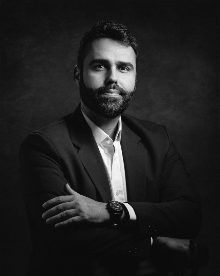 Retrato de Thiago Bomfim, de terno e braços cruzados.