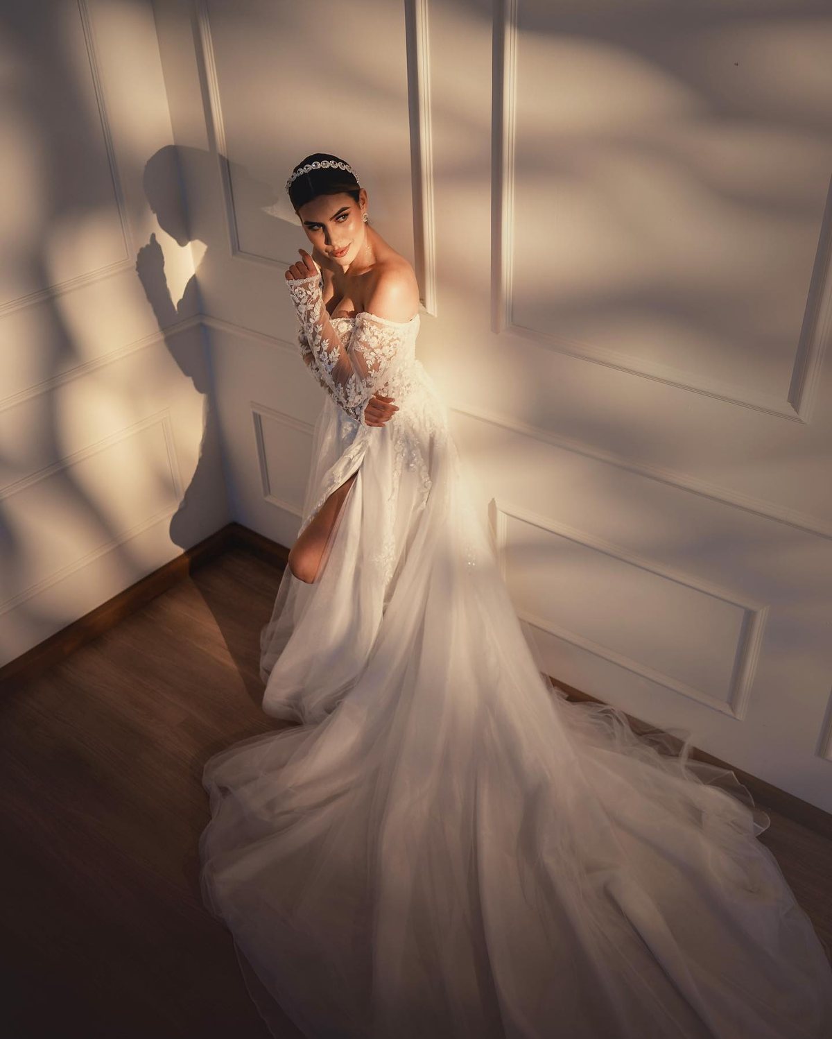 Noiva de vestido de renda com cauda longa, com luz de janela na parede de boiserie