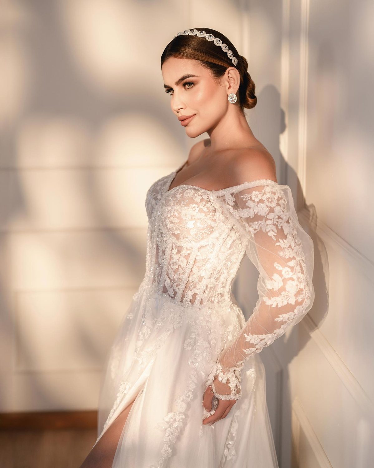 Noiva de vestido de renda com ombros à mostra e tiara, com luz recortada de janela