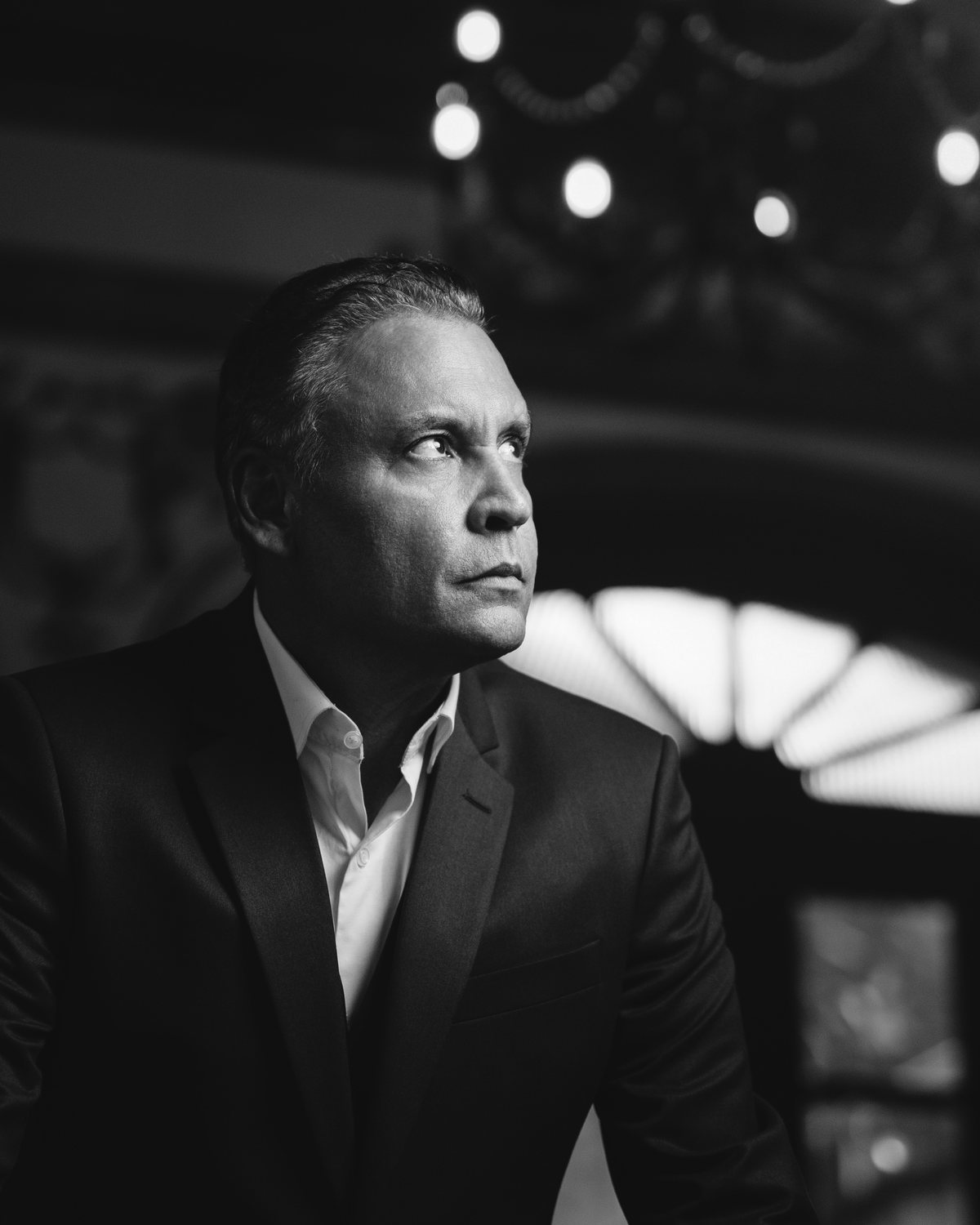Retrato masculino em preto e branco, de perfil, com luzes desfocadas ao fundo