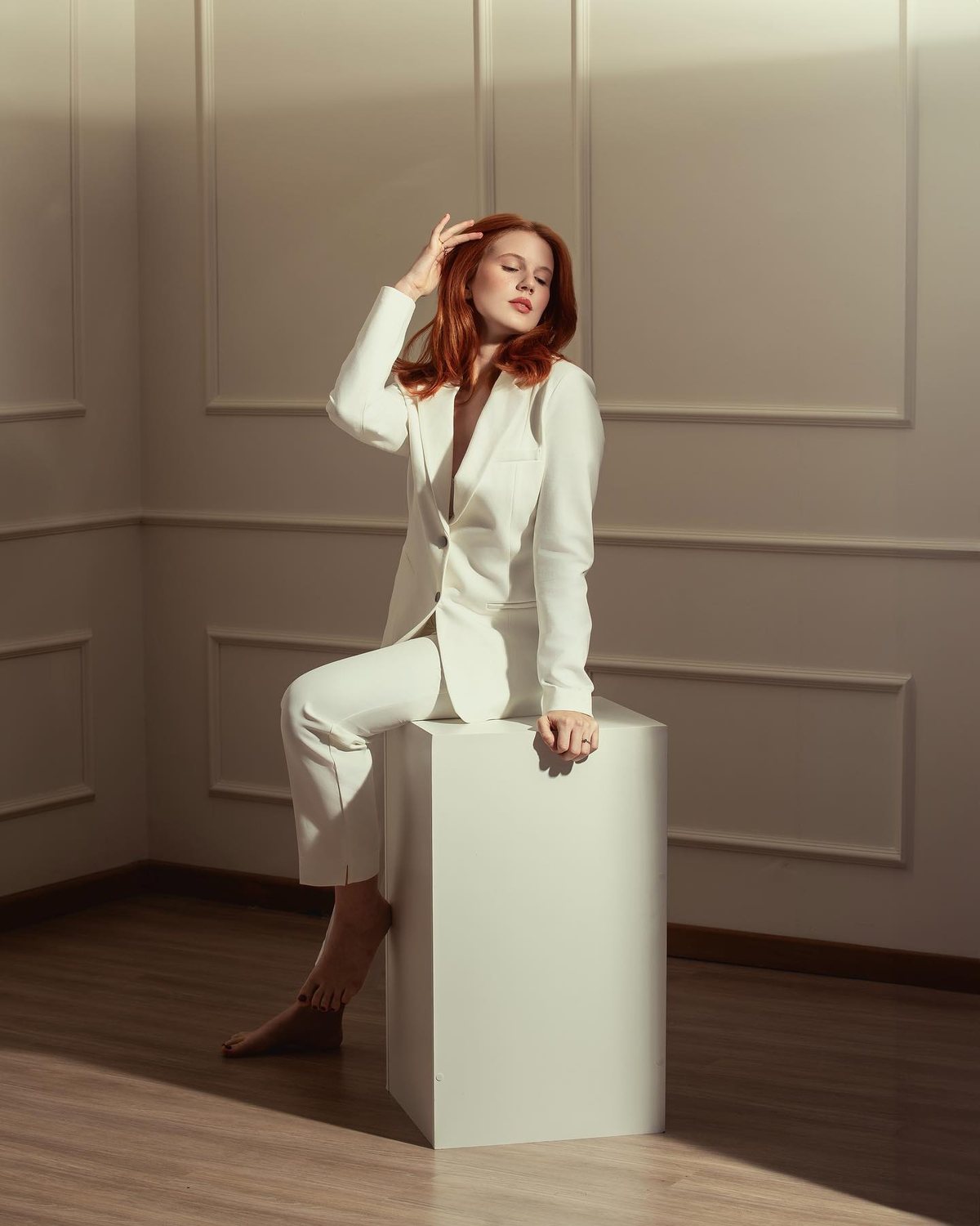 Resultado do desafio: mulher ruiva de terno branco sentada num cubo branco, diante da boiserie