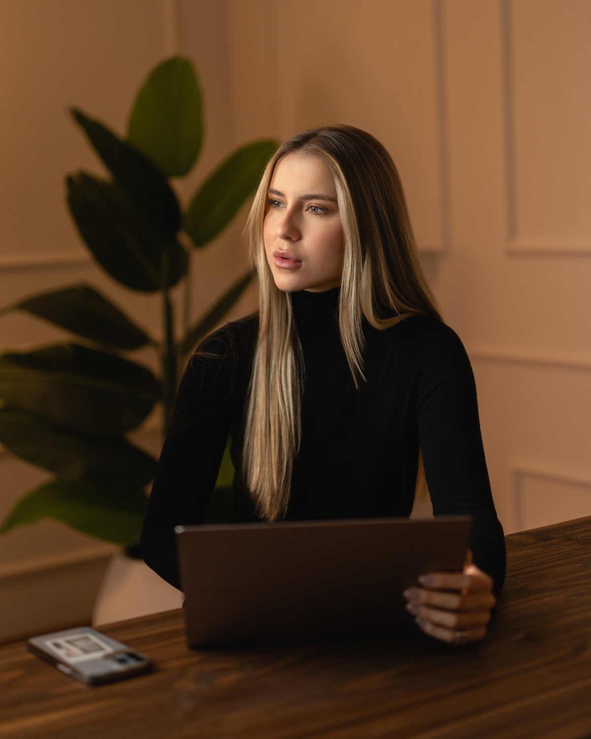 Executiva à mesa com notebook, planta ao fundo e luz quente