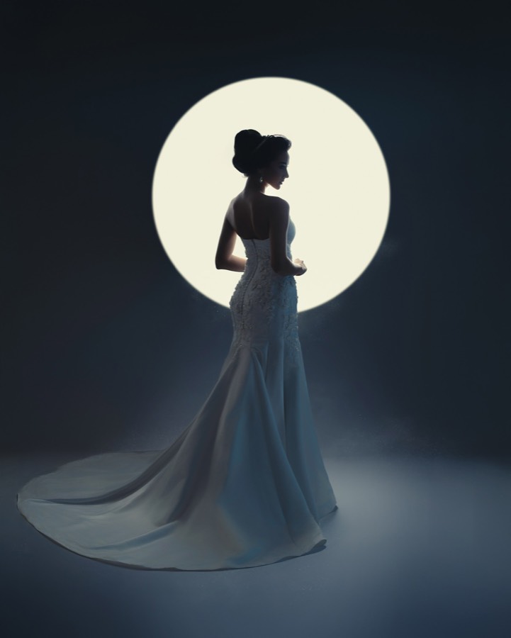Silhueta de vestido longo contra um círculo de luz.